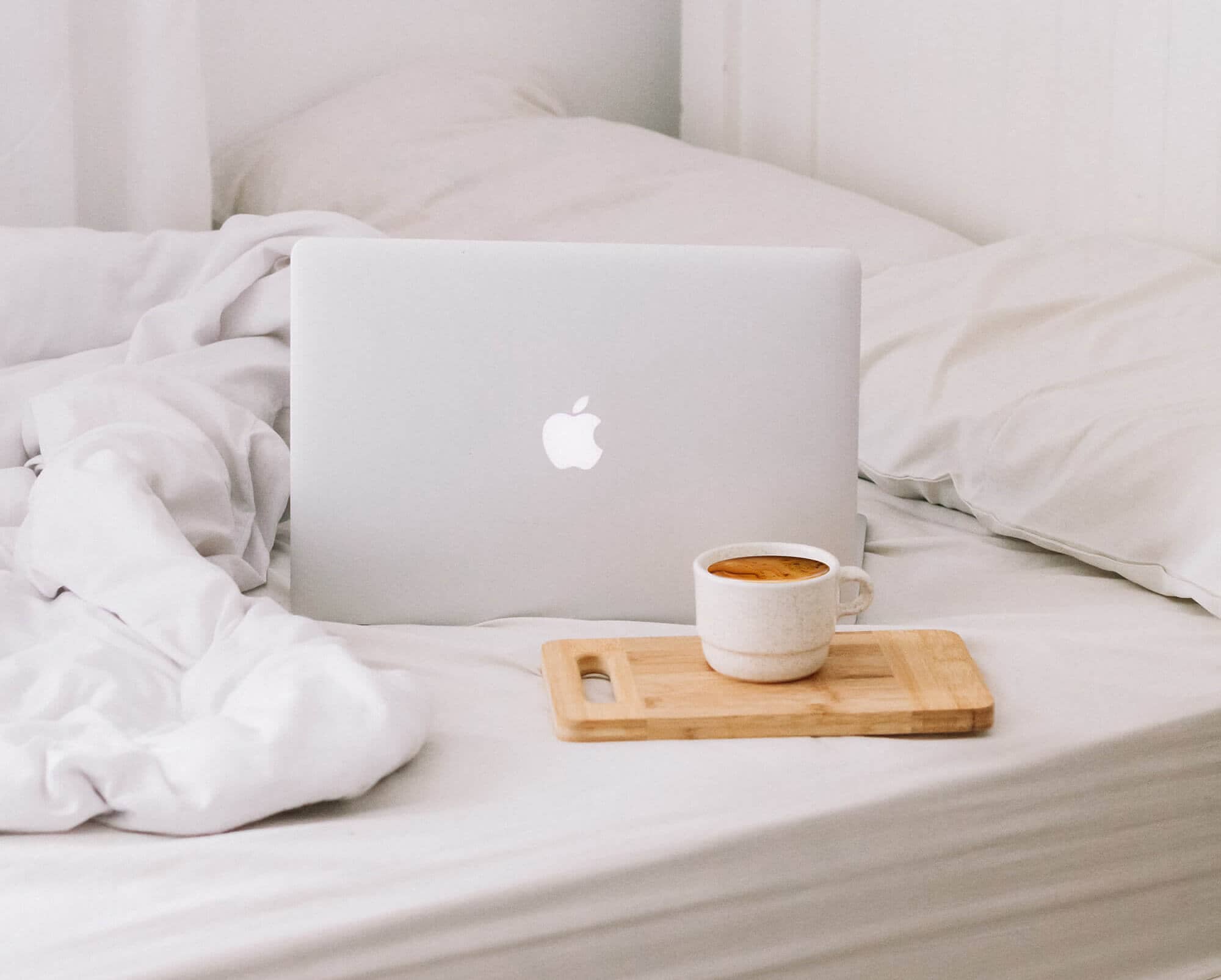 Laptop on a bed with a cup of coffee in front